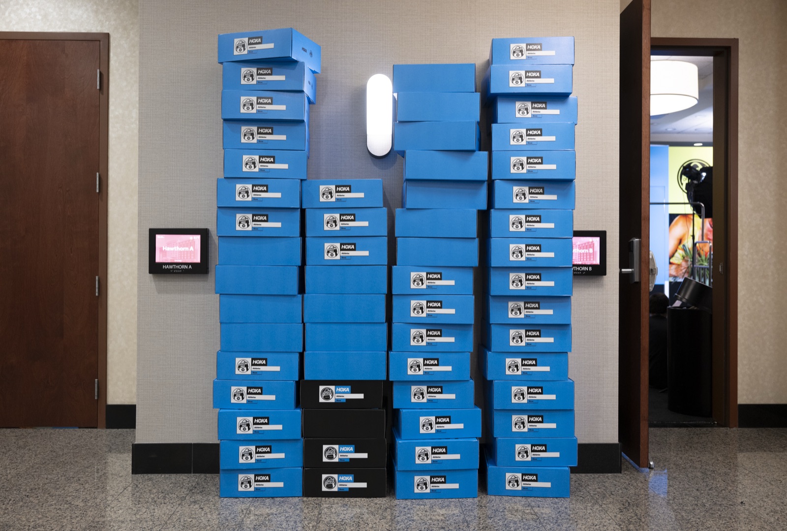 Custom-printed HOKA athlete shoe boxes, labeled by athlete and shoe, stacked at the team hotel