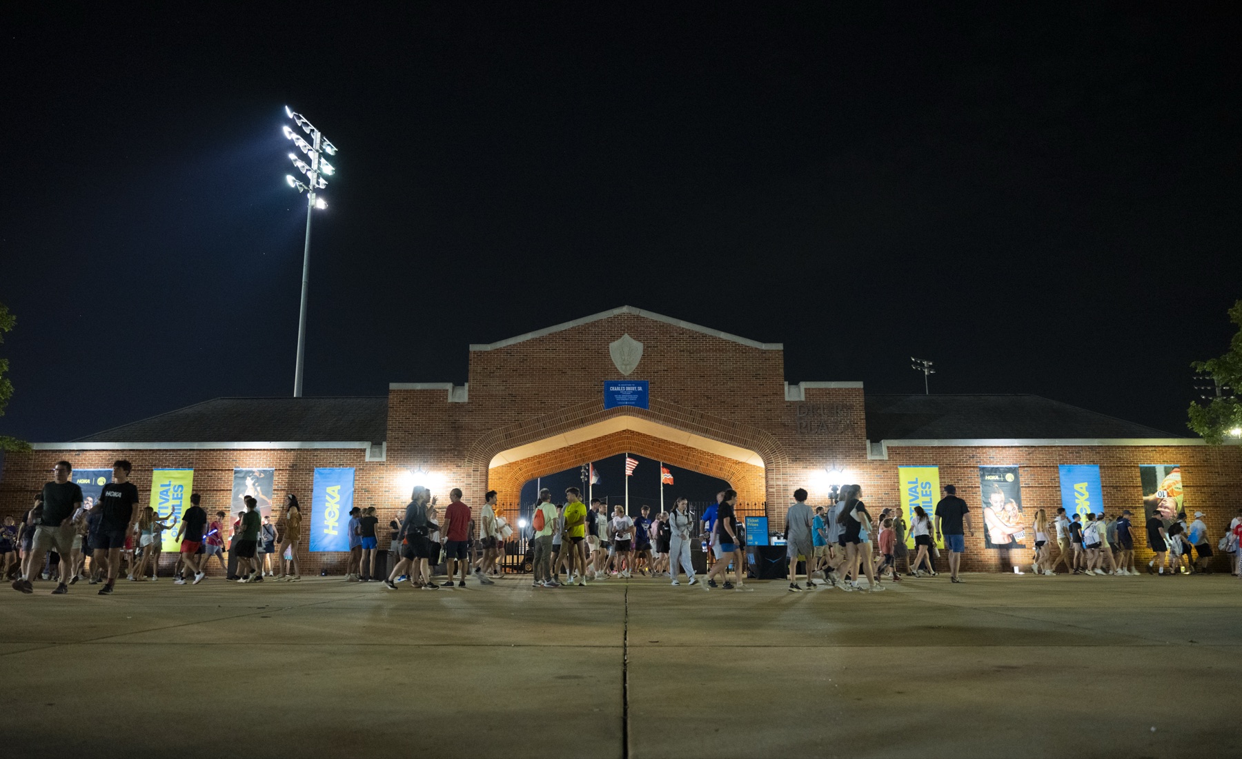 Stadium gates at night lined with HOKA and Festival of Miles banners as crowds leave the meet