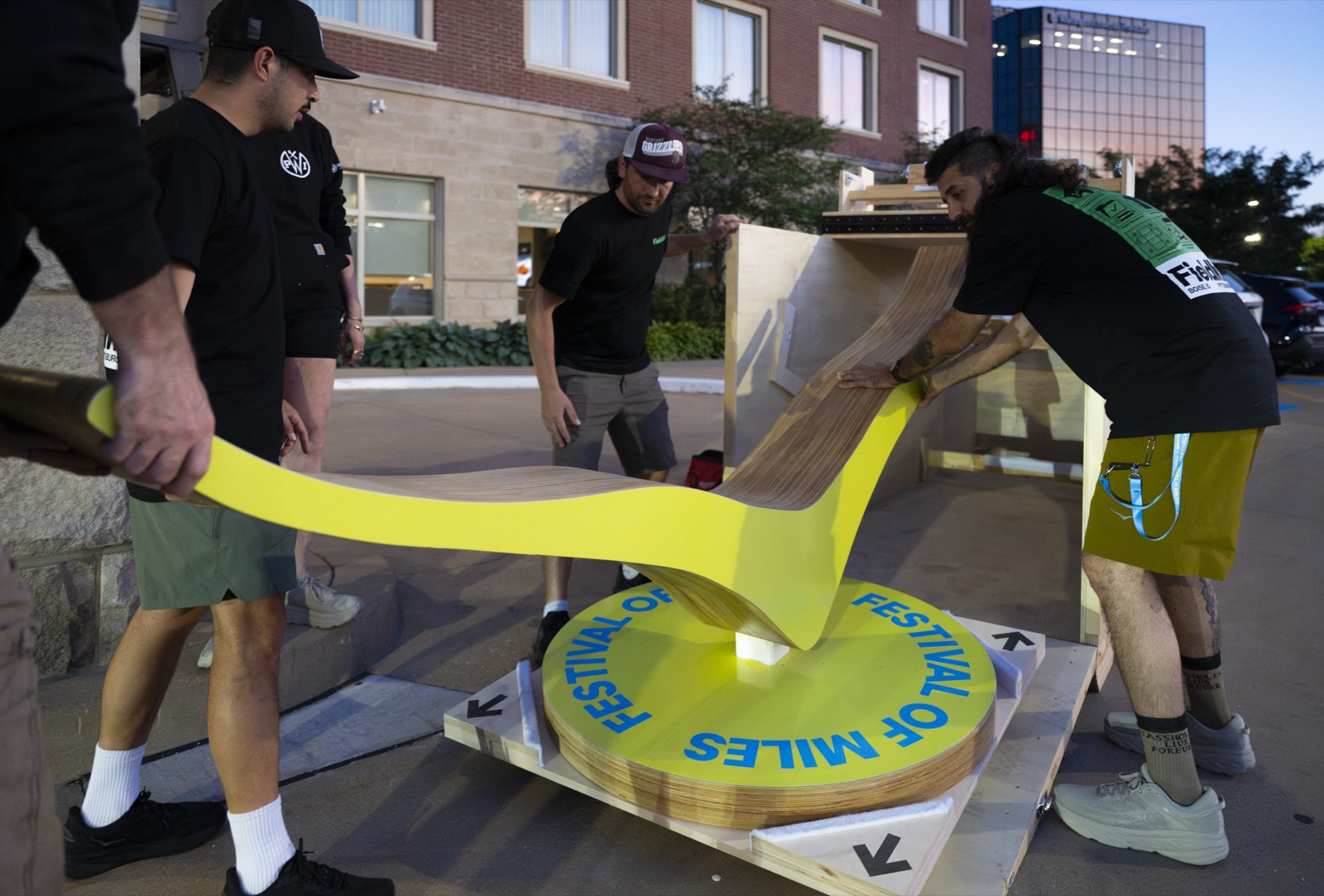 Fieldkit crew assembling the laminated-plywood HOKA wing sculpture onto its printed base outside the venue